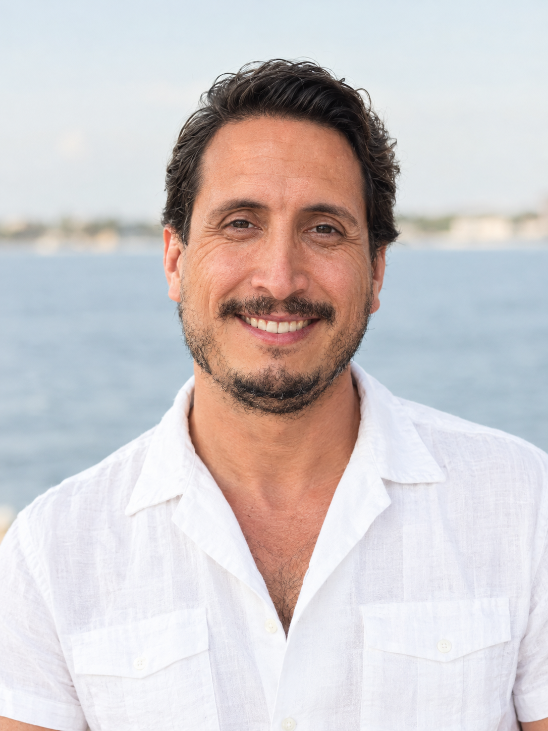 Christian Ramirez, founder of Twenty Seven Books, smiling in a white linen shirt beside the sea